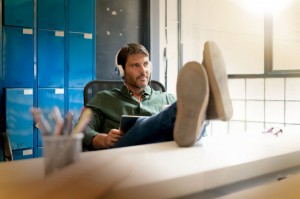 man-wearing-headphones-working-in-modern-office-with-feet-up-on-desk_69315-730